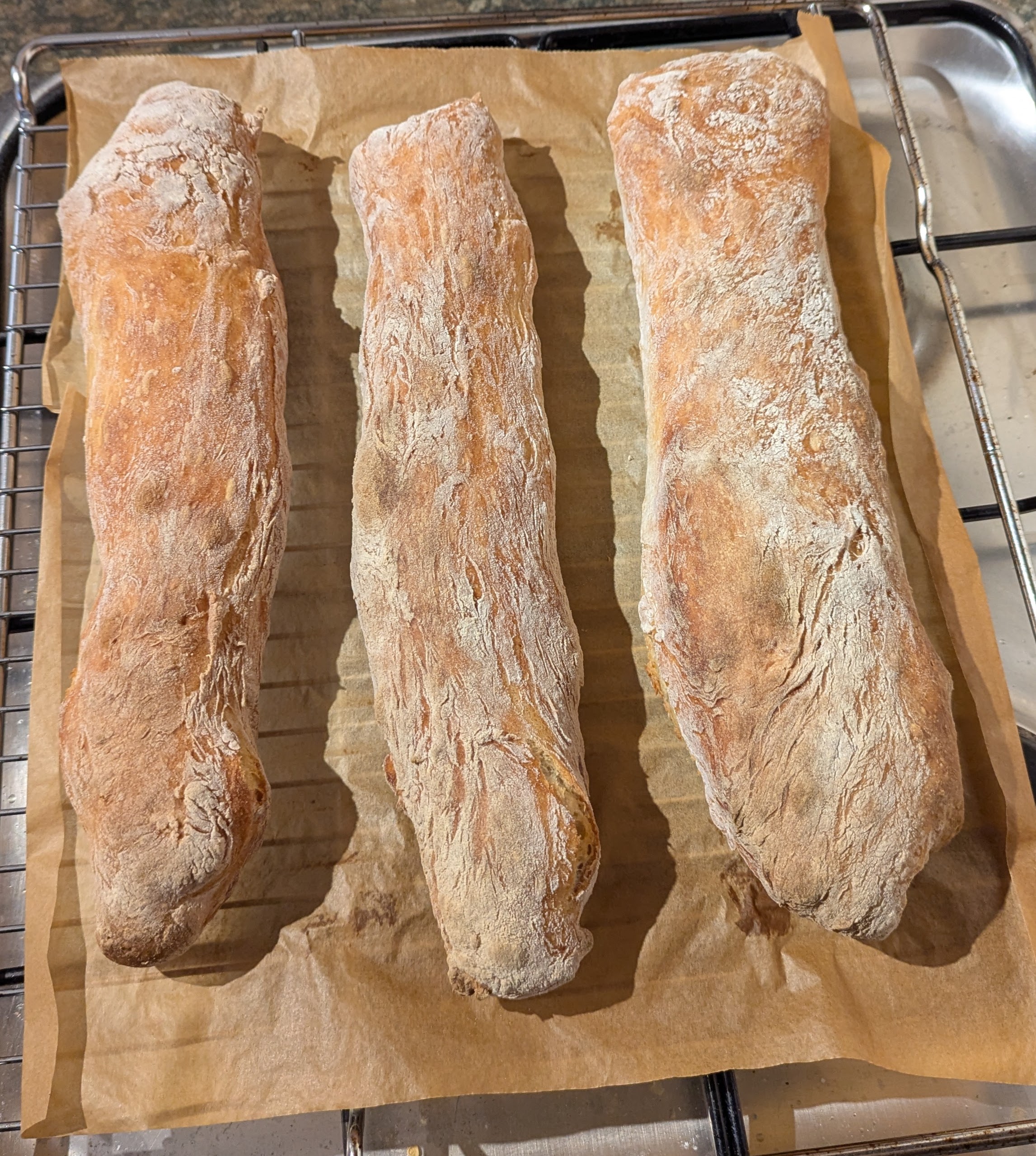 Three lovely fresh baguettes on a rack fresh out of the oven.