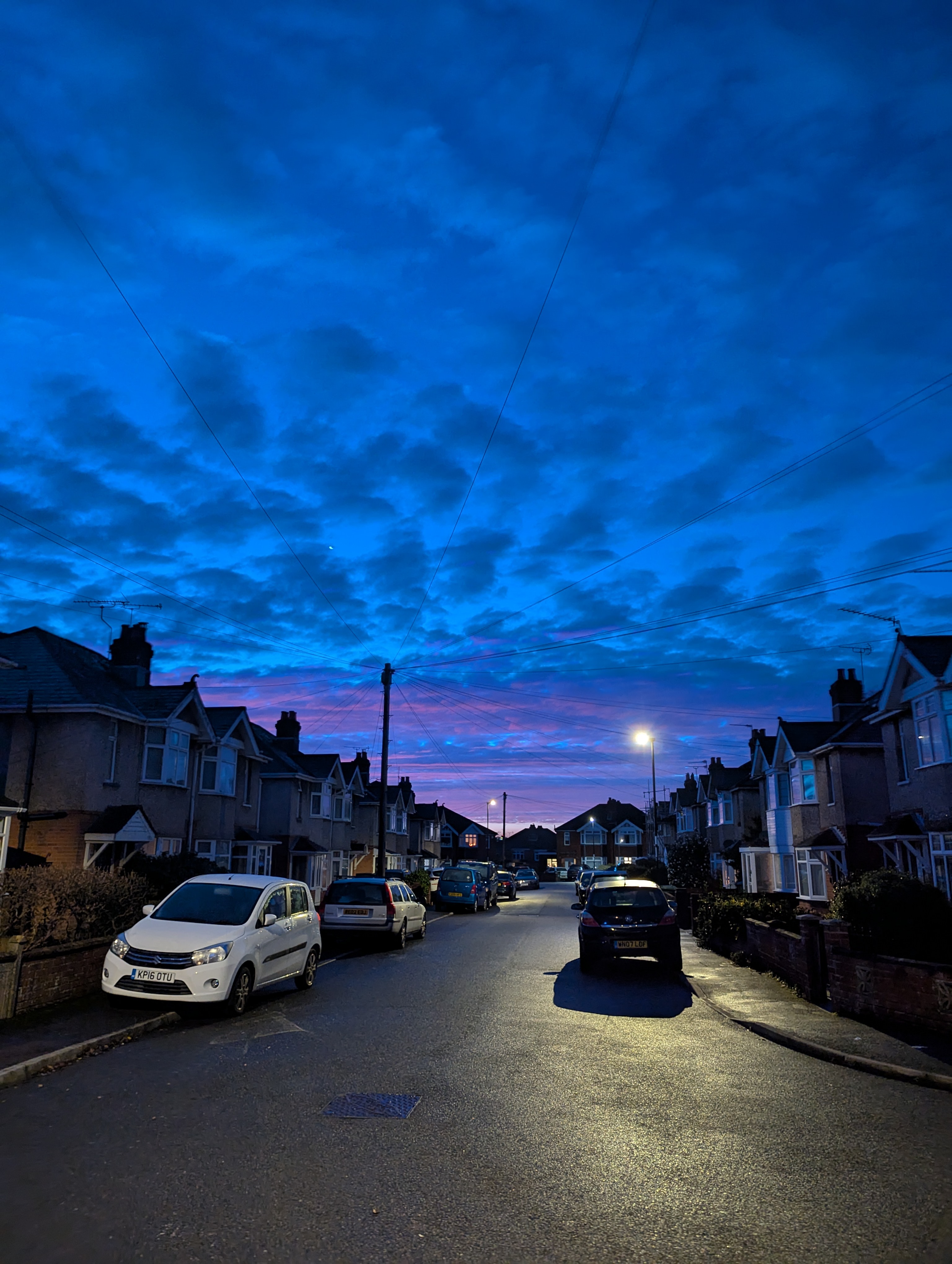 A photo the sunset in Southampton on 16th December 2025. It shows a road with parked cars and terraced houses and blue/violet sky with traces of clouds, oranges and pinks.