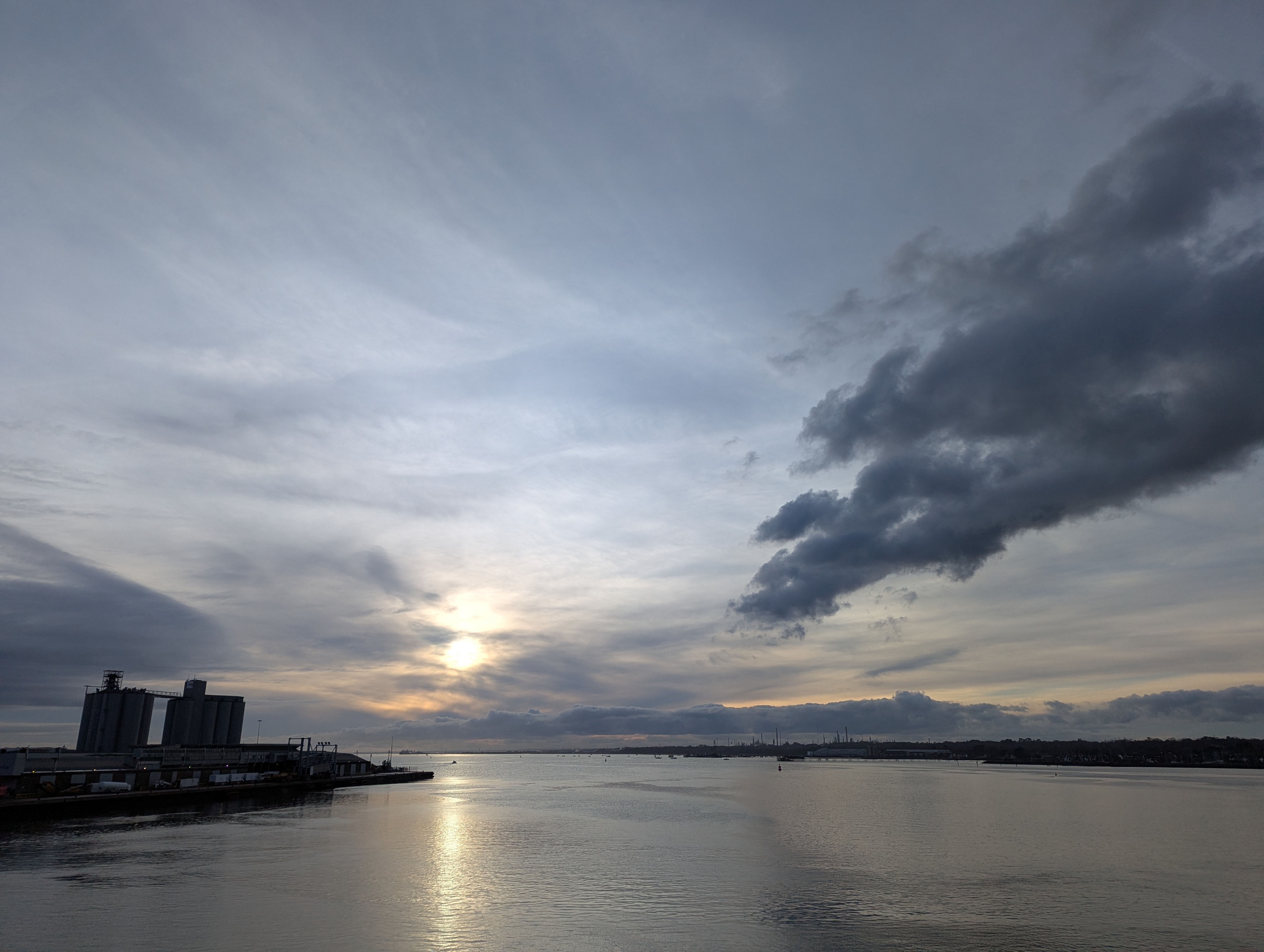 A veiw of the sun rising over the Solent with pale clouds on a still day in December.